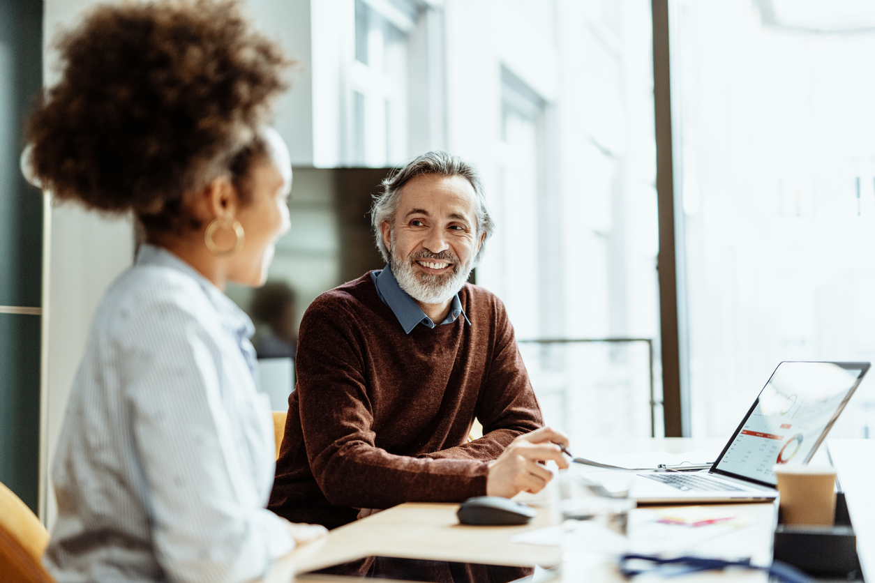 Smiling financial advisor and business person talking to mixed race female colleague in office